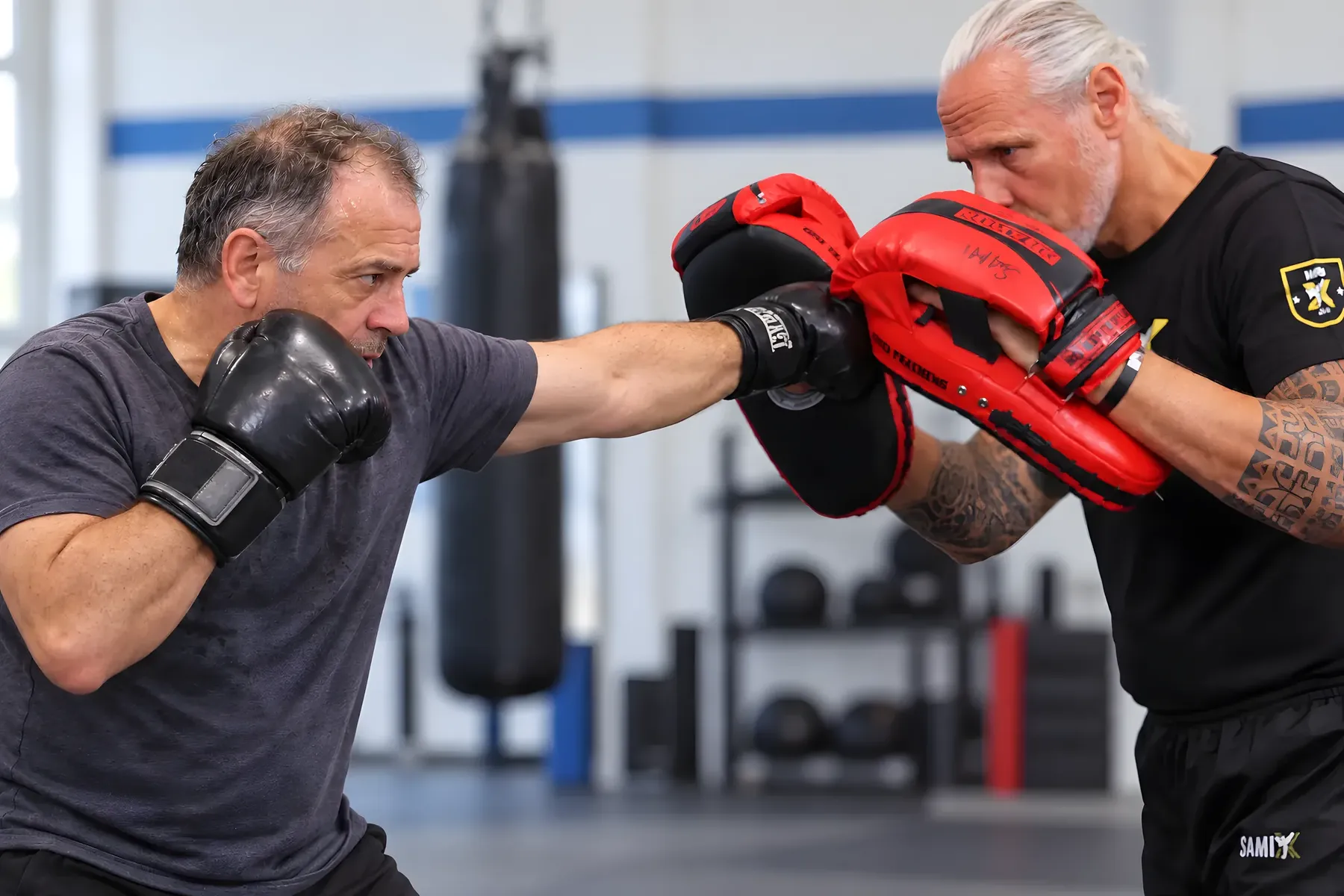 Ein Mann schlägt mit Boxhandschuhen auf die Pratzen seines Coaches