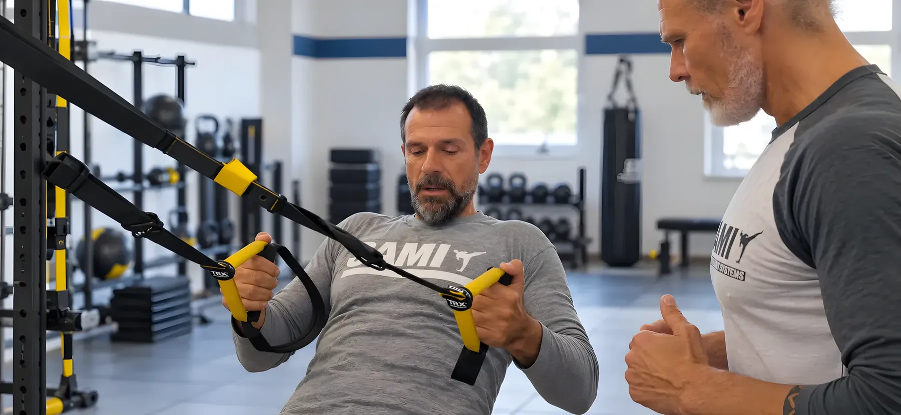 Ein Mann zieht sich am Schlingentrainer hoch, sein Coach gibt Hinweise