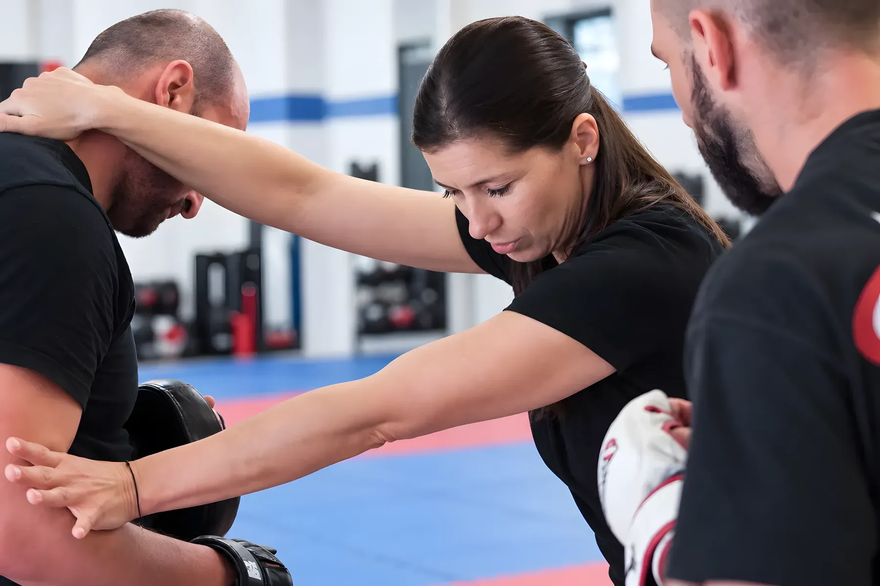 Eine Frau bei einer Partnerübung mit zwei Trainingspartnern und Schlagpolster